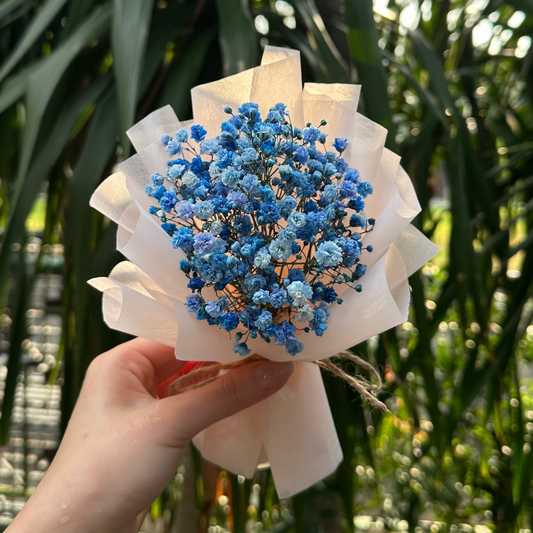 Hand holding a small bouquet of blue flowers with greenery in the background