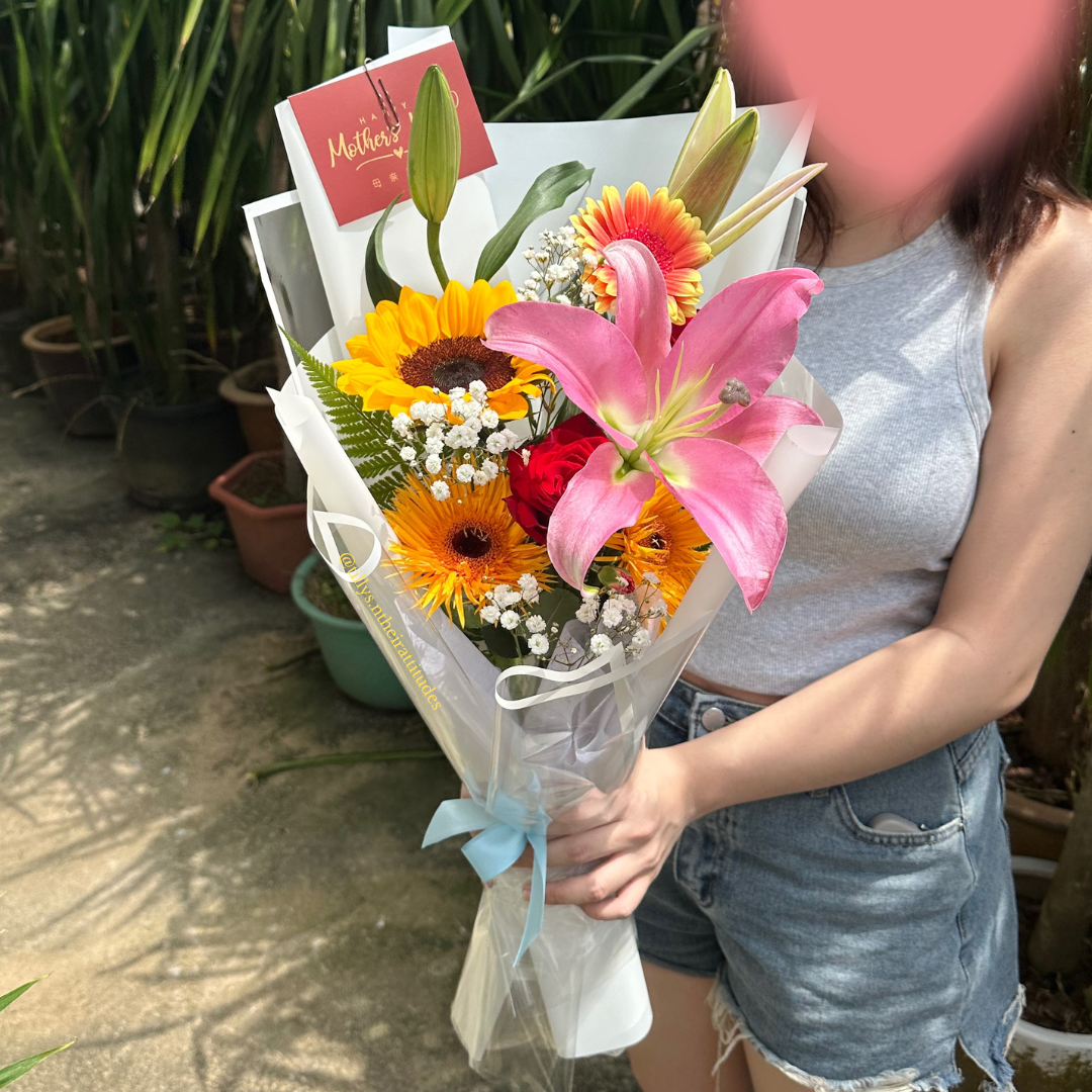 Person holding a bouquet of flowers with a 'Mother's Day' card in a garden setting.